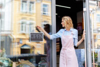 female shop owner setting up an "open" sign (Depositphotos)