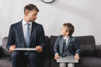 Young boy and man, both wearing suits, sitting next to each other (Depositphotos)