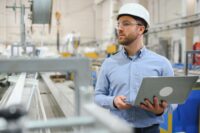 Side view of technician or engineer with headset and laptop standing in industrial factory by Depositphotos